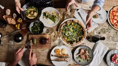 This is a photo of people enjoying a food spread of pizza, asparagus, fish, bread, olives and wine at the Wilding restaurant in Oxford.