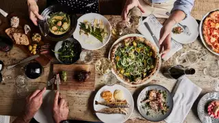 This is a photo of people enjoying a food spread of pizza, asparagus, fish, bread, olives and wine at the Wilding restaurant in Oxford.